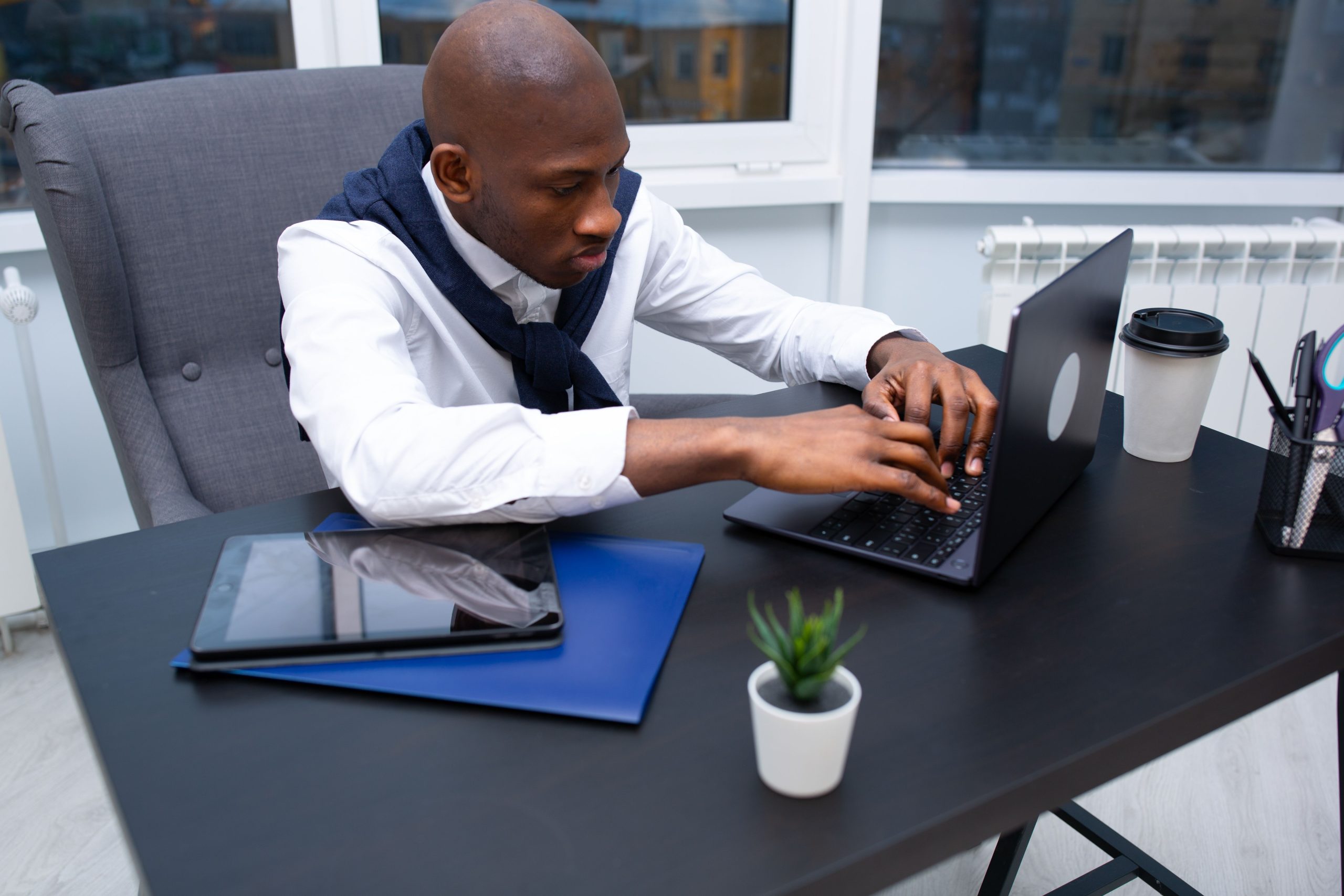 Black man in a white shirt using a laptop at a modern office desk.